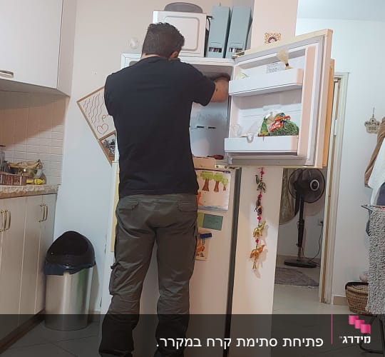 אדם מתקן מקרר עם דלת פתוחה וכלי עבודה
